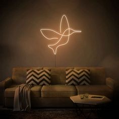 a living room with a couch, coffee table and neon bird sculpture on the wall