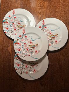 four plates with birds and flowers on them sitting on a wooden table next to a glass vase