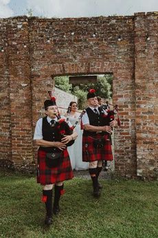 two men in kilts are playing bagpipes near an old brick wall and doorway