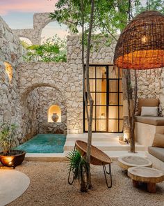 an outdoor hot tub surrounded by stone walls and trees with lights on the ceiling above it