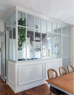 a dining room table and some chairs in front of a glass case with plants on it