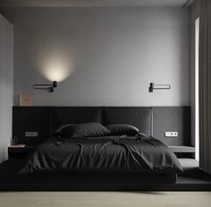 a bed with black sheets and pillows in a room next to a wall mounted light