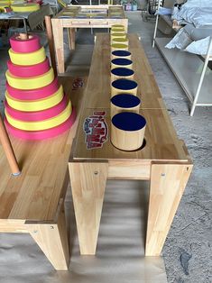 a wooden table with several different colored bowls on it and some chairs in the background