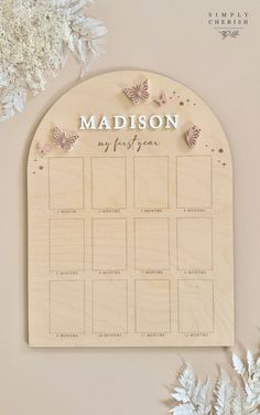 a wooden calendar with butterflies on it and the word madison written in white ink, next to some flowers