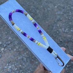 a hand holding a beaded necklace in a box with a pair of scissors on it