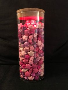 a glass filled with lots of pink and purple candies next to a black background