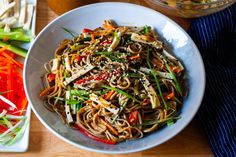 a white bowl filled with noodles and veggies on top of a wooden table