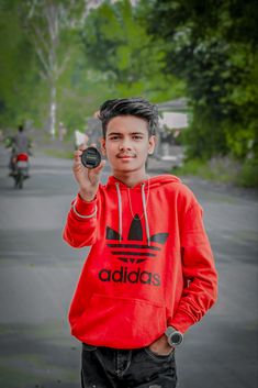 a young boy in a red adidas hoodie holding up a cell phone