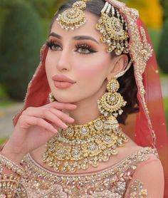 a woman in a bridal outfit with jewelry on her neck and hands near her face