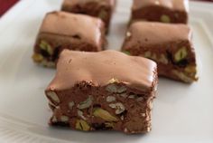 four pieces of chocolate dessert on a white plate with almonds and pistachio