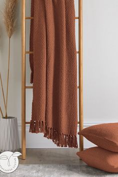 a brown blanket sitting on top of a wooden stand next to pillows and a vase