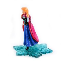 a frozen princess figurine standing on top of a blue piece of plastic ice