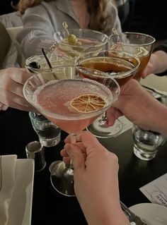 several people holding up wine glasses filled with different types of drinks and garnishes