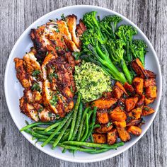 a white plate topped with chicken, broccoli and sweet potato wedges next to green beans