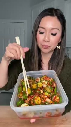 a woman holding chopsticks over a container of food