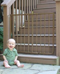 a baby sitting on the ground in front of a stair railing and door to a house