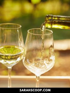 two wine glasses filled with white wine being poured