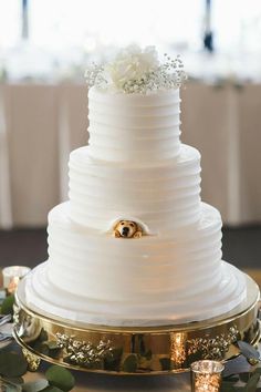 a three tiered white wedding cake on a gold plate with greenery around it