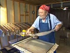 a man in an apron and bandana is using a large knife to cut something