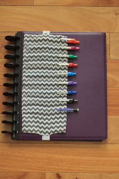 a notebook with markers on it sitting on a wooden floor next to a pen holder