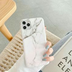 a woman's hand holding up a white marble phone case