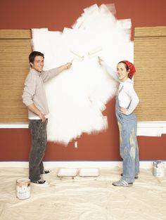 a man and woman standing in front of a white wall with paint rollers on it