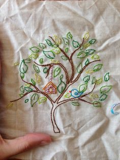 a hand embroidered tree with two birds and a birdhouse in the center, on a white cloth