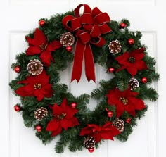 a christmas wreath with poinsettis and pine cones hanging on a white door