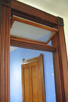 a mirror with a wooden frame and blue walls in the background, reflecting an open door