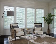 a living room filled with furniture and large windows covered in white shuttered shades on the windows