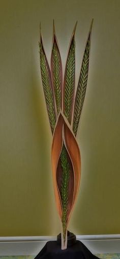 a vase with leaves on it sitting on a black tablecloth covered floor in front of a green wall