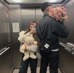 a man taking a selfie with a woman holding a teddy bear in an elevator