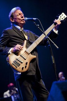 a man in a suit and tie playing a bass guitar on stage with other musicians behind him