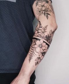 a man with a tattoo on his arm holding onto a piece of paper that has flowers and leaves on it