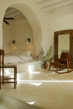 a bedroom with a bed, mirror and rocking chair in front of an arched doorway