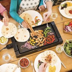 several people sitting at a table with plates of food and drinks on it, including tortillas