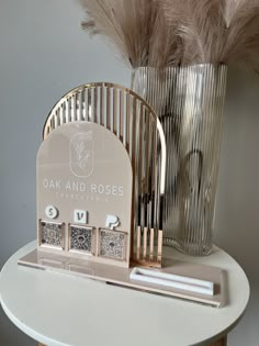 a white table topped with a metal vase filled with feathers and an electronic device sitting on top of it