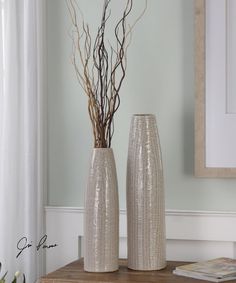 two silver vases sitting on top of a wooden table