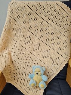 a crocheted blanket with a teddy bear sitting on the chair next to it