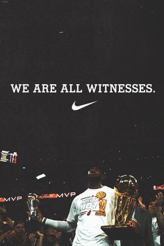 a man standing in front of a crowd holding a trophy with the words we are all witnesses above him