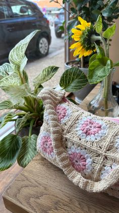 a crocheted purse sitting on top of a wooden table next to a vase filled with flowers