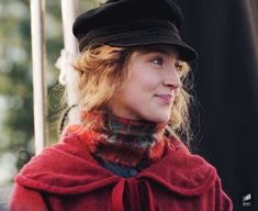 a woman wearing a black hat and red coat with a plaid scarf around her neck