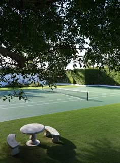 a tennis court with benches and a table in the middle of it, surrounded by green grass