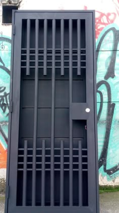 a black door with bars on it in front of a graffiti covered wall