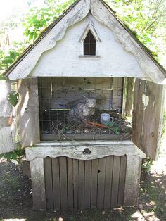 an outdoor hut with a bird in it's cage on the ground next to a fence