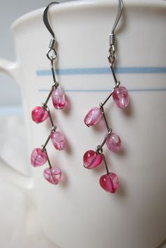 a pair of pink glass beaded earrings sitting on top of a white coffee cup