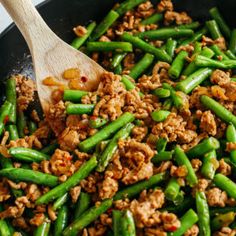 green beans and meat in a skillet with a wooden spatula on the side