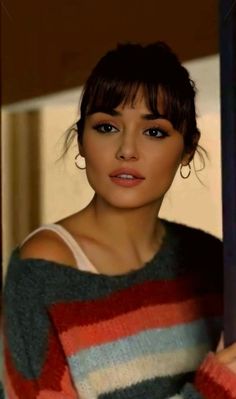 a woman with short hair wearing a colorful sweater and hoop earrings looking at the camera