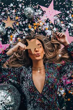 a woman holding a star in front of her face with confetti all around her