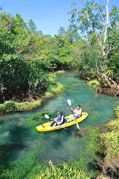 two people in a kayak paddling down a river filled with clear blue water